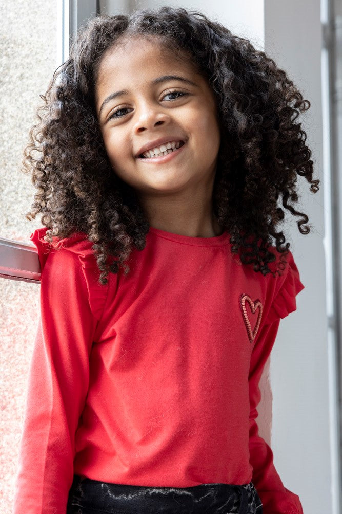 Dieses rote Langarmshirt aus der Queen Of Hearts Kollektion von Jubel besticht durch ein kleines Herzmotiv und verspielte Rüschen an den Ärmeln. Es verbindet Komfort mit einem charmanten Design, das jeden Tag verschönert.