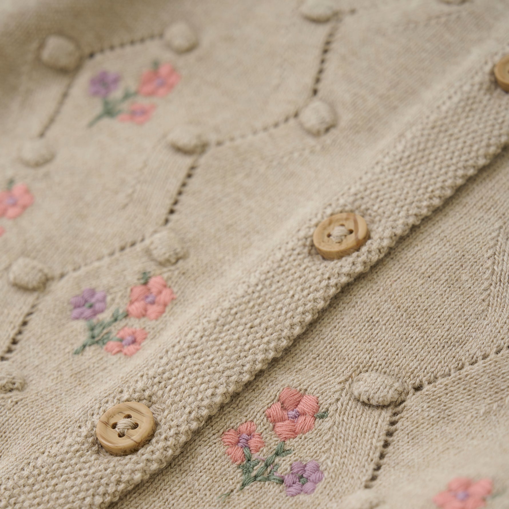 Der beige Cardigan von MINYMO besticht durch seine sorgfältig gearbeiteten Blumenverzierungen und verbindet zeitloses Design mit liebevollen Details.
