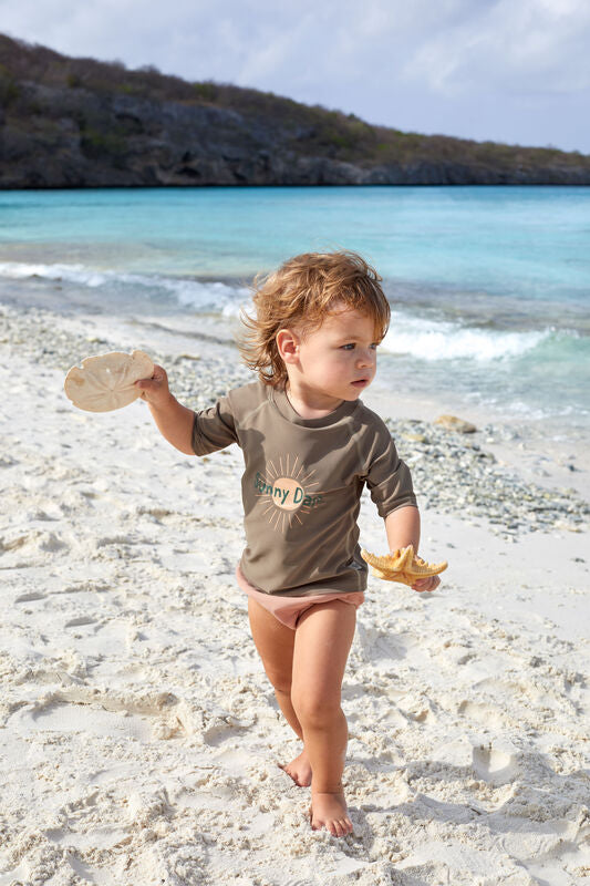 Das braune, kurzärmelige Kinder UV Shirt mit UV-Schutz 60 kommt mit dem Sonnen Print und extra weichem Stoff. Das atmungsaktive und schnelltrocknende Material sorgt für eine angenehme Passform und Badespaß.