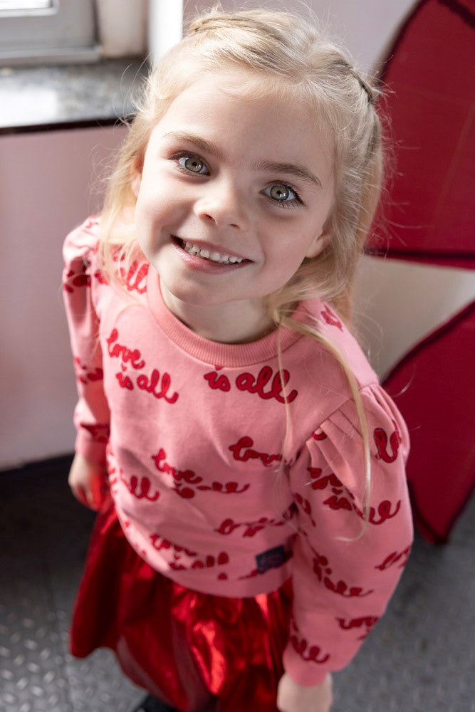 Dieser rosa Pullover aus der Queen Of Hearts Kollektion von Jubel besticht durch seinen auffälligen roten All-Over-Print und verleiht jedem Outfit einen einzigartigen Charme.