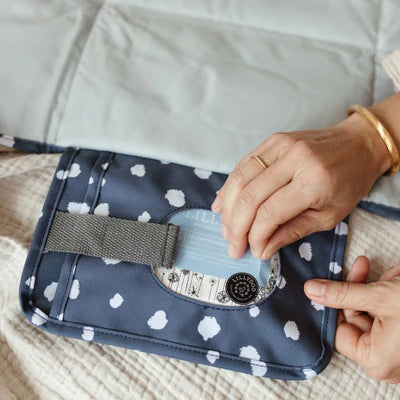 Die Wickelunterlage mit blauen Punkten ist ideal für unterwegs. Sie lässt sich einfach am Handgelenk oder Kinderwagen befestigen und bietet dank Innentaschen Platz für Windeln und Pflegeartikel. Nach Gebrauch wird sie kompakt zusammengefaltet, sodass Du jederzeit schnell und hygienisch wickeln kannst.