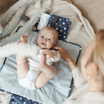 Die Wickelunterlage mit blauen Punkten ist ideal für unterwegs. Sie lässt sich einfach am Handgelenk oder Kinderwagen befestigen und bietet dank Innentaschen Platz für Windeln und Pflegeartikel. Nach Gebrauch wird sie kompakt zusammengefaltet, sodass Du jederzeit schnell und hygienisch wickeln kannst.
